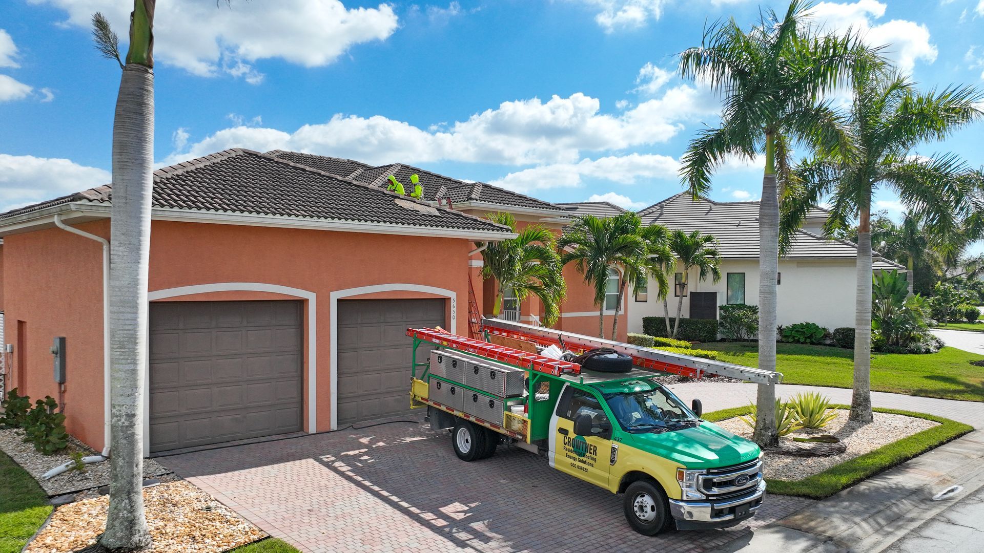 Green utility truck parked in front of a peach house with palm trees and a garage