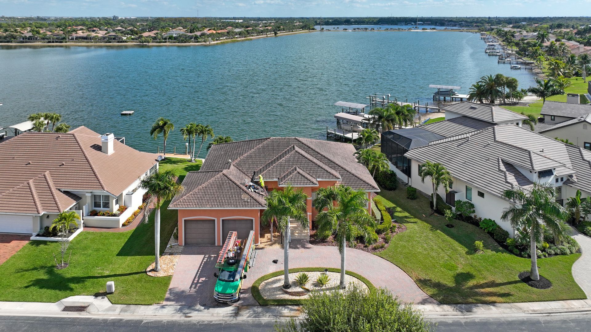 Aerial view of lakeside homes with docks, palm trees, and a blue waterfront under a clear sky
