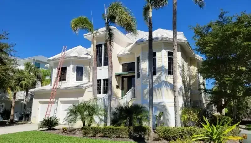 White multi-story house with palm trees and lush landscaping under a bright blue sky