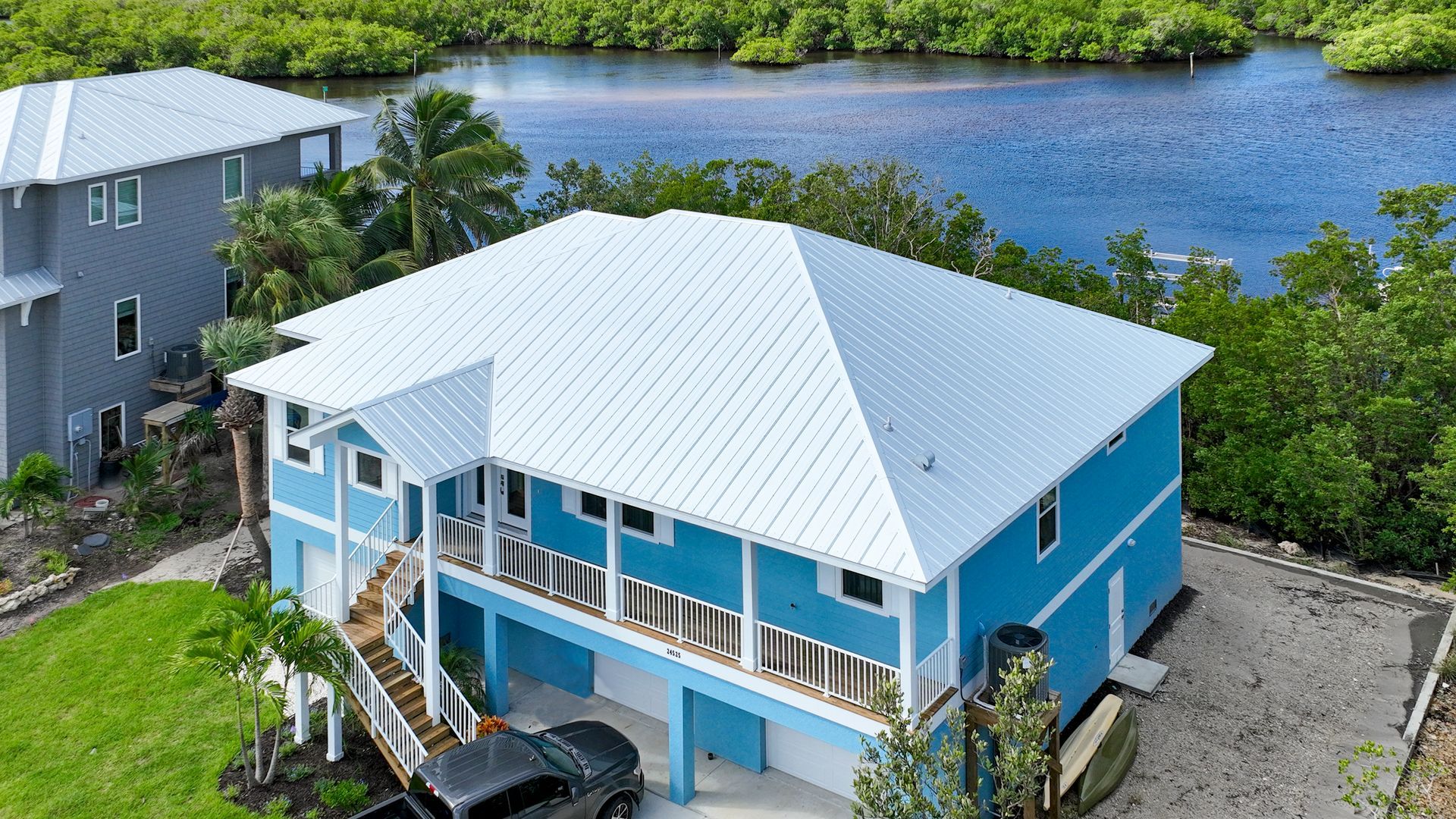 Blue waterfront house with white roof, blue balcony, and garage beside a river.
