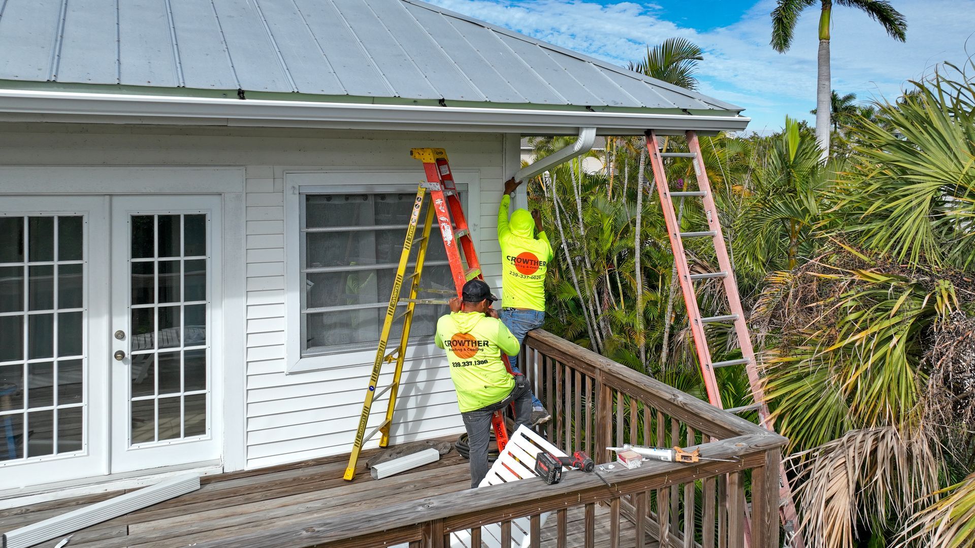 Construction workers on a tiled roof under a blue sky, wearing yellow safety gear