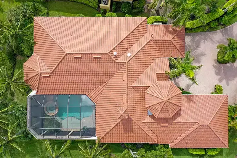 Aerial view of a terracotta-roofed house surrounded by lush greenery, with a screened pool enclosure.