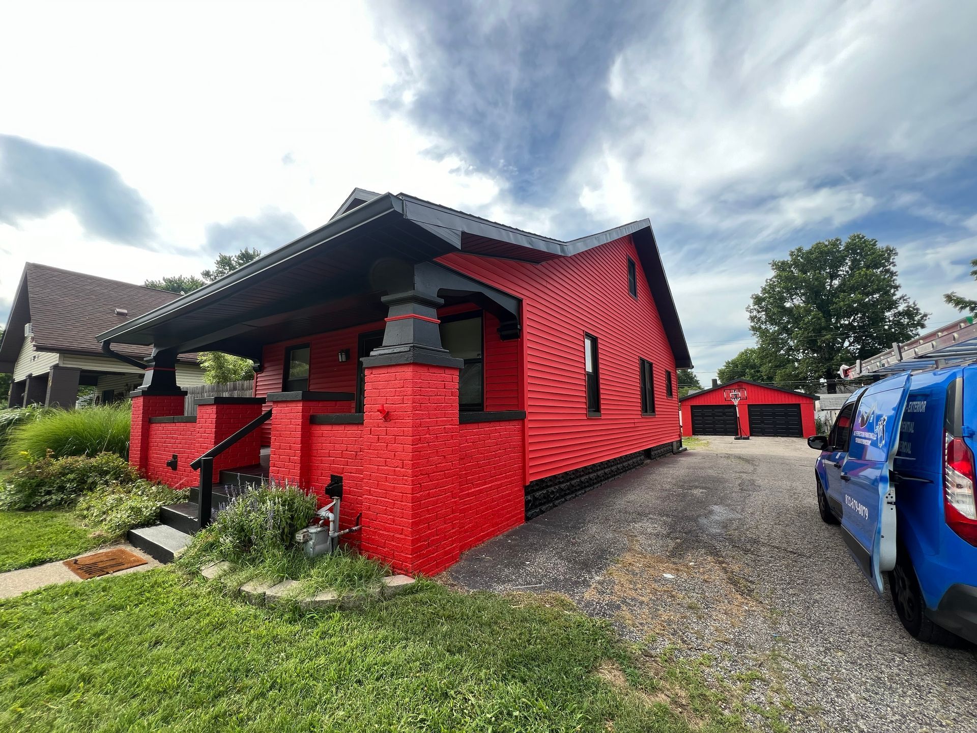 Red house with black trim under a cloudy sky. A blue van is parked in the driveway.