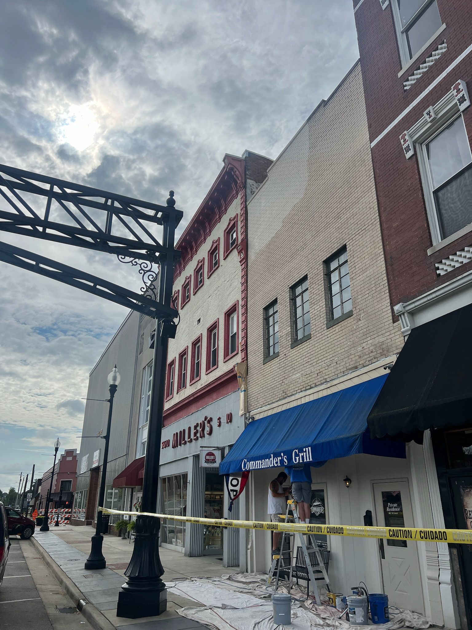 Street view with several buildings. Construction activity in front of a white building with a blue awning. Cloudy sky.