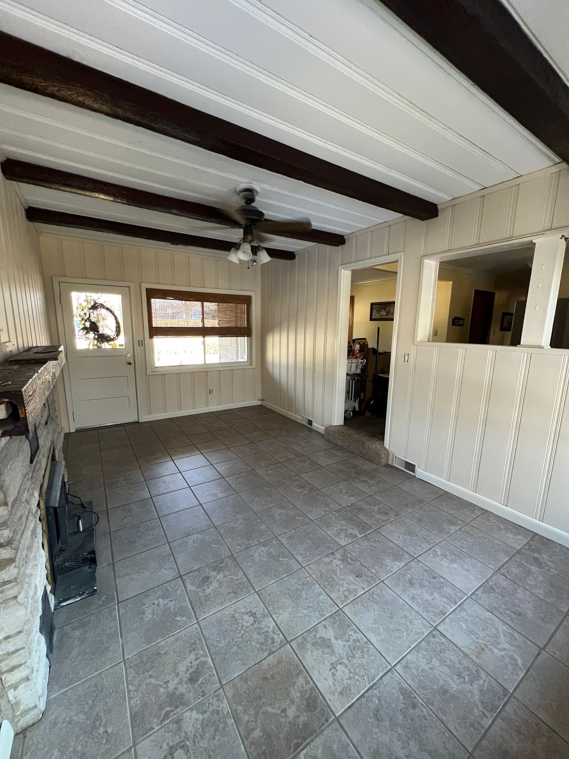 Interior view: Living room with tile floor, white paneled walls, dark beams, and a brick fireplace.