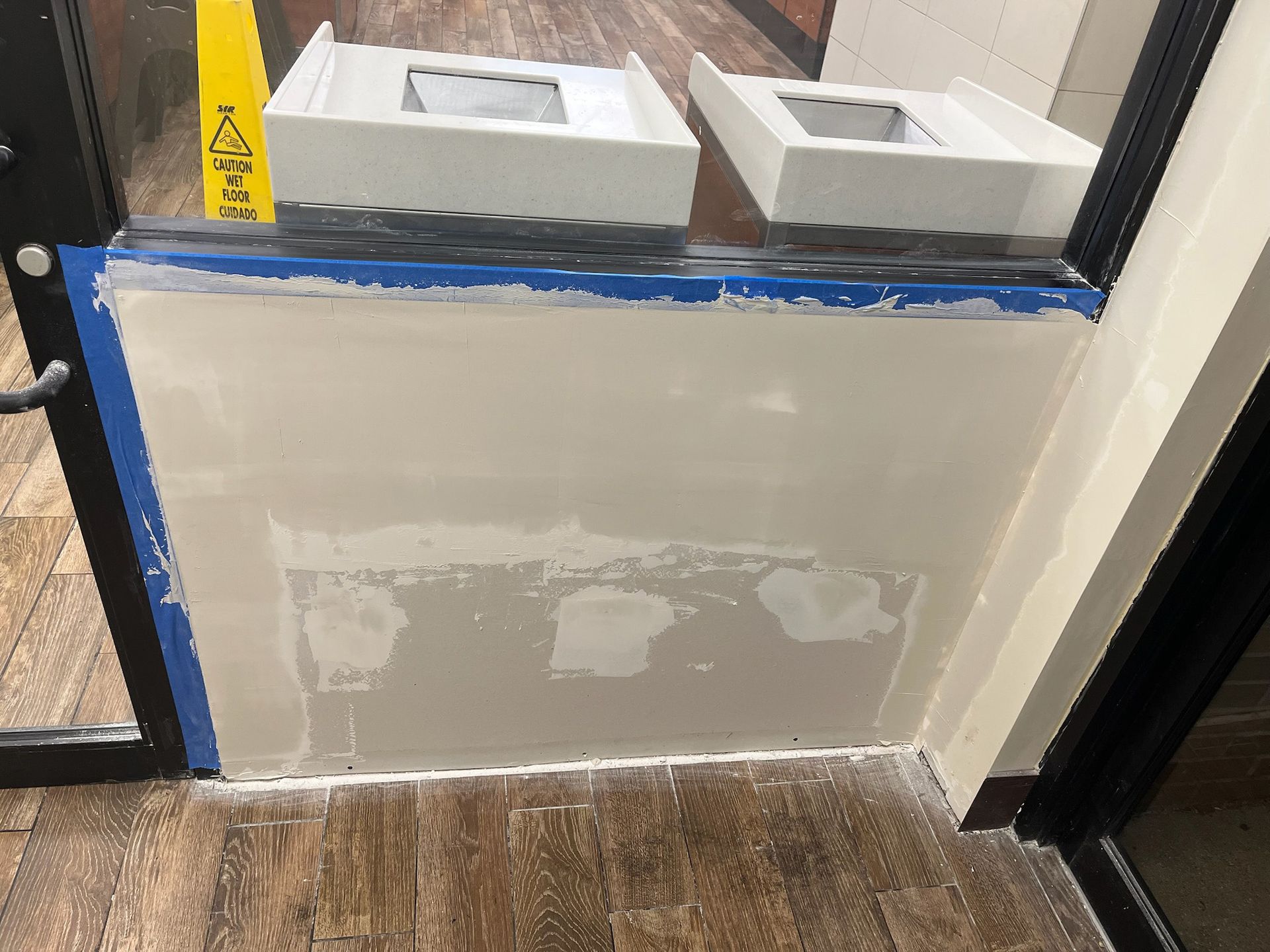 Wall repair in progress; blue tape, wet plaster, wet floor.