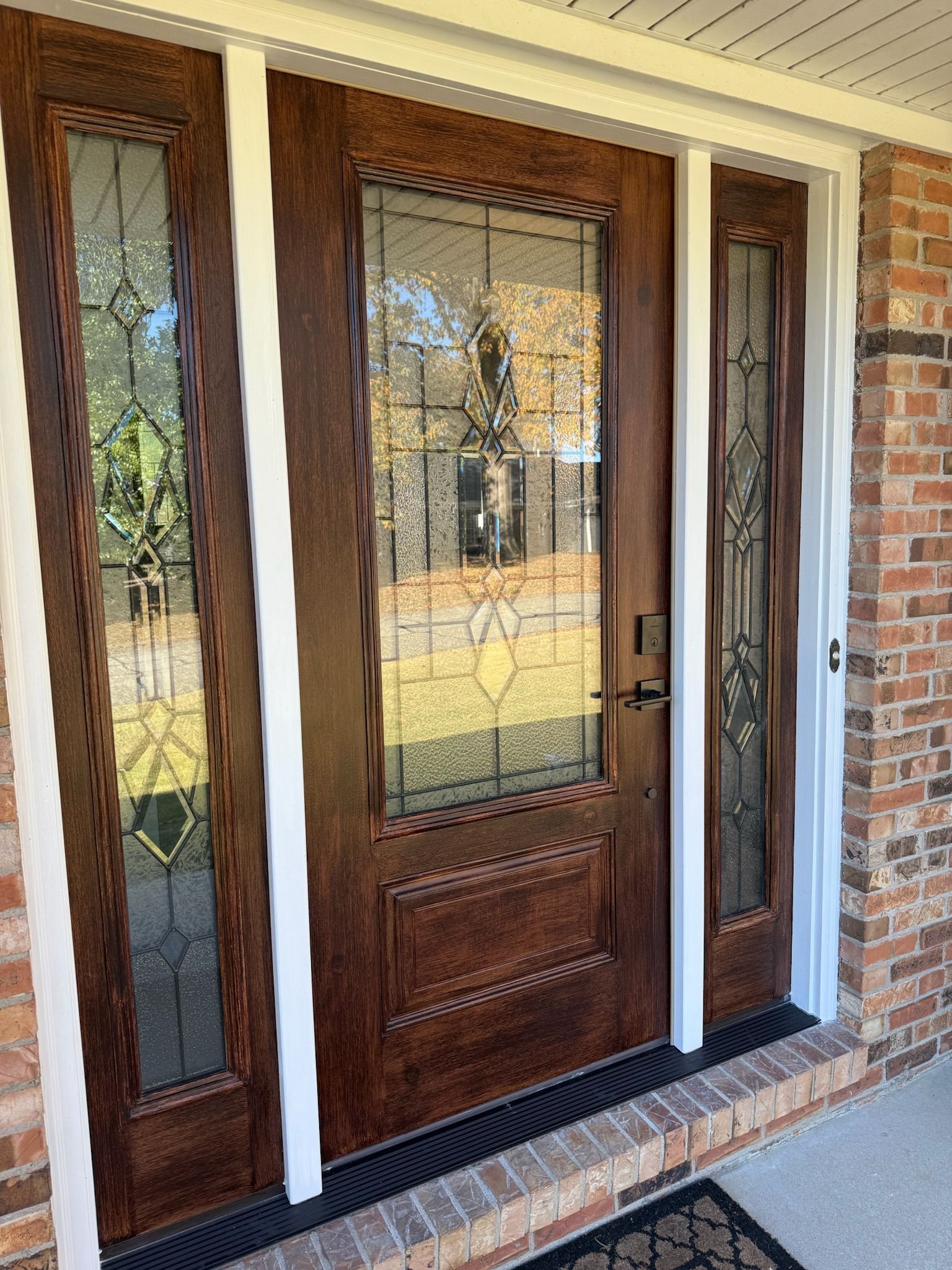 Wooden front door with stained glass panels, framed by white trim on brick house.
