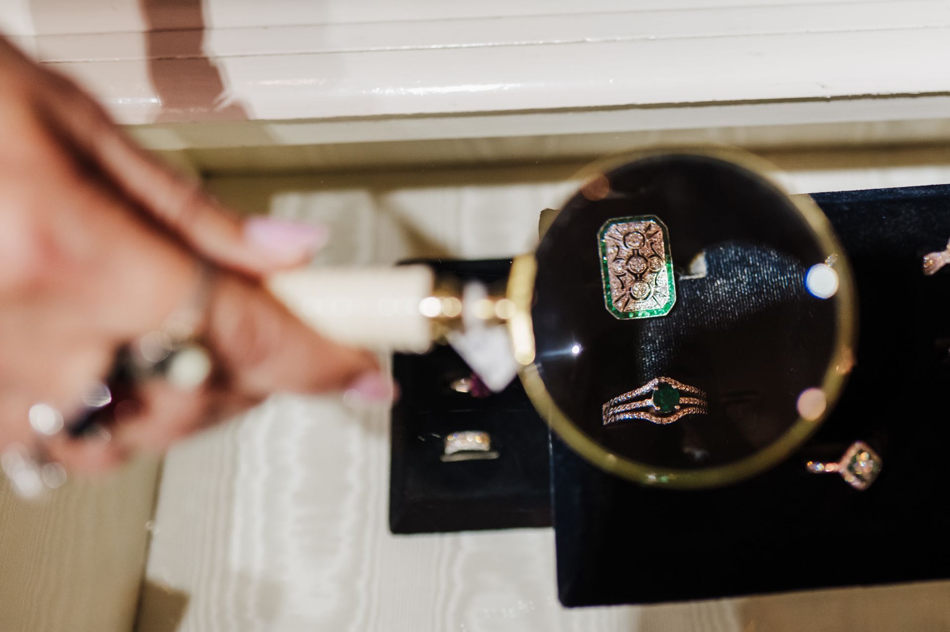 A Hand Hols a Magnifying Class Inspecting Fine Jewelry at McAdams, a Columbia, MO Gift Store.