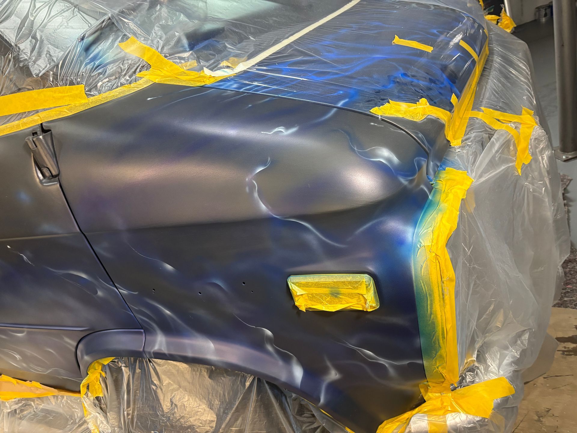 Blauw carrosseriepaneel afgeplakt met plastic en tape ter voorbereiding op het schilderen.