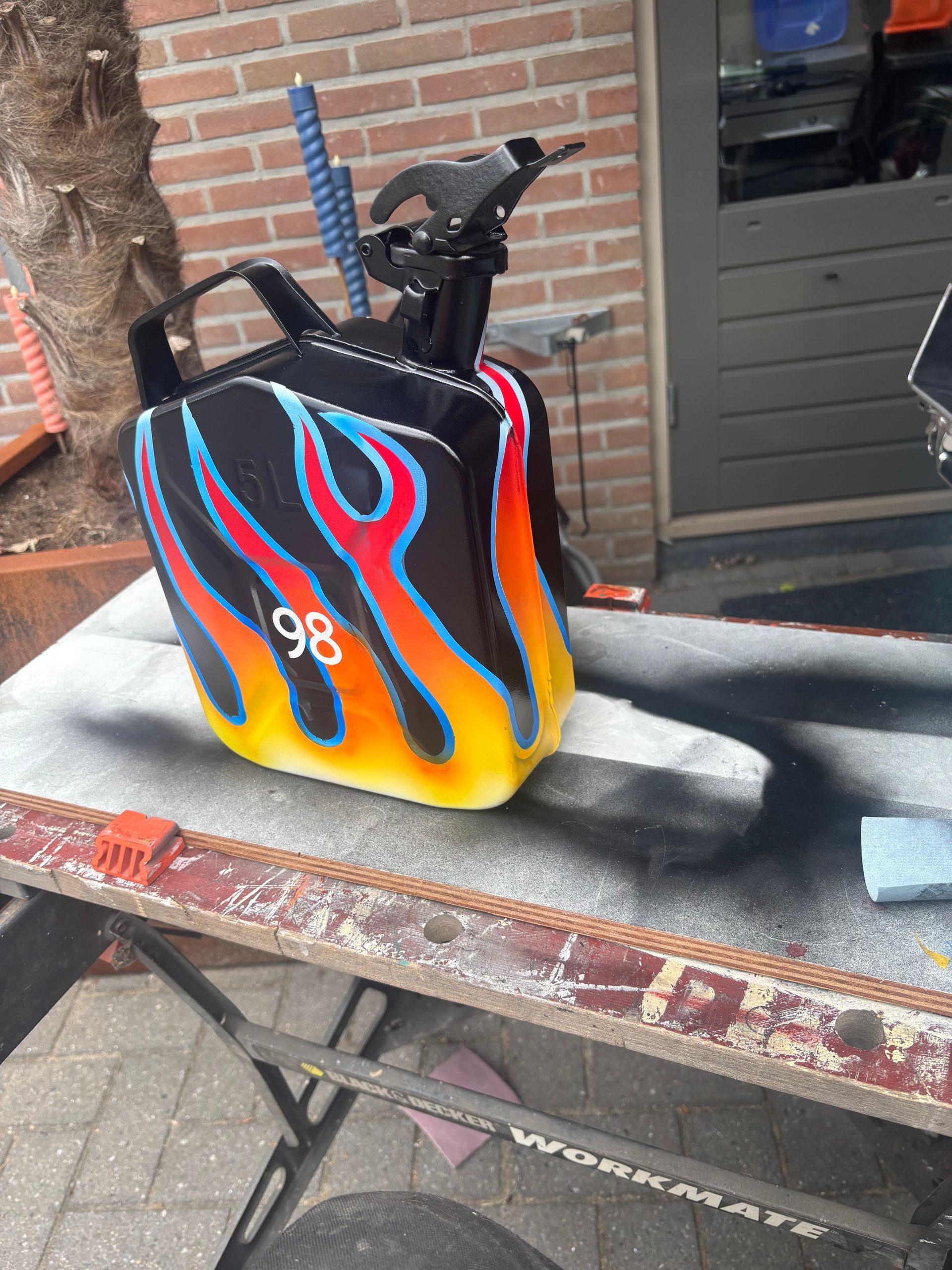 Kleurrijk beschilderde racehelmtas met vlammen en nummer 98 op een werkbank buiten.