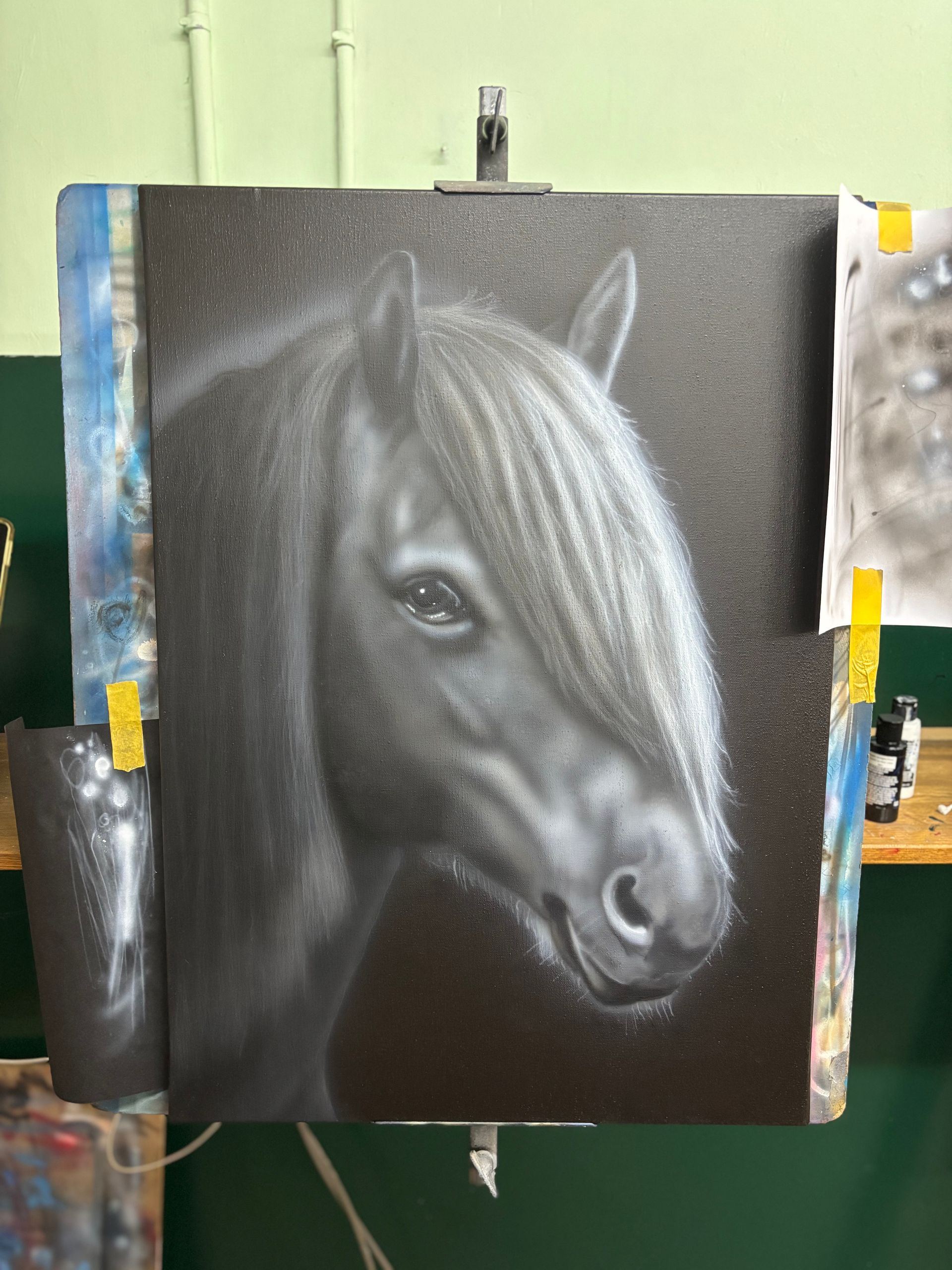 Houtskooltekening van een paardenhoofd met lange manen op zwart papier, tentoongesteld op een schildersezel.