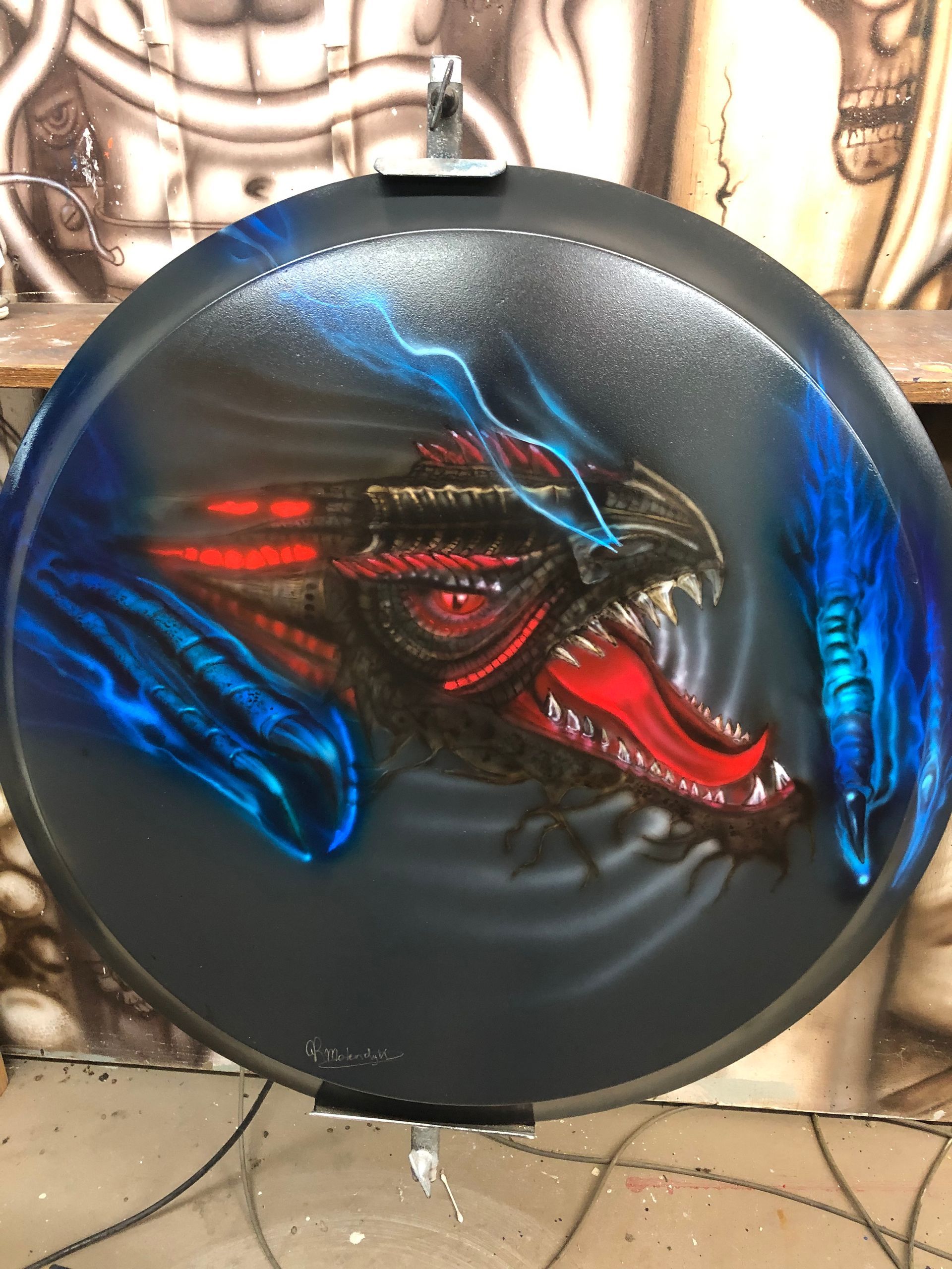 Rond zwart wanddecoratie met een rood-blauwe, grommende draak op een zwarte achtergrond.