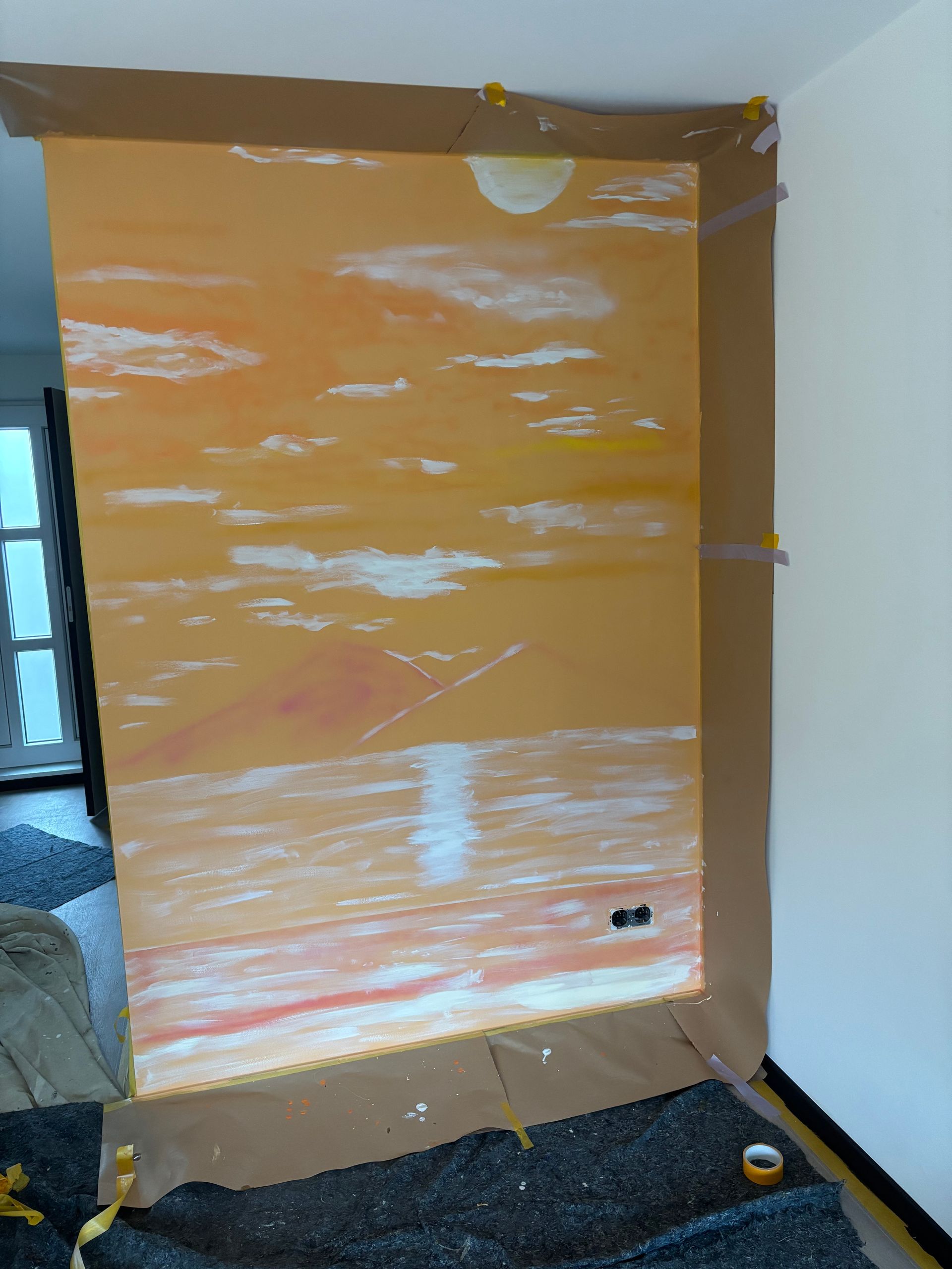 Een oranje muurschildering met wolken en de zon is op een muur in een binnenkamer geplakt.