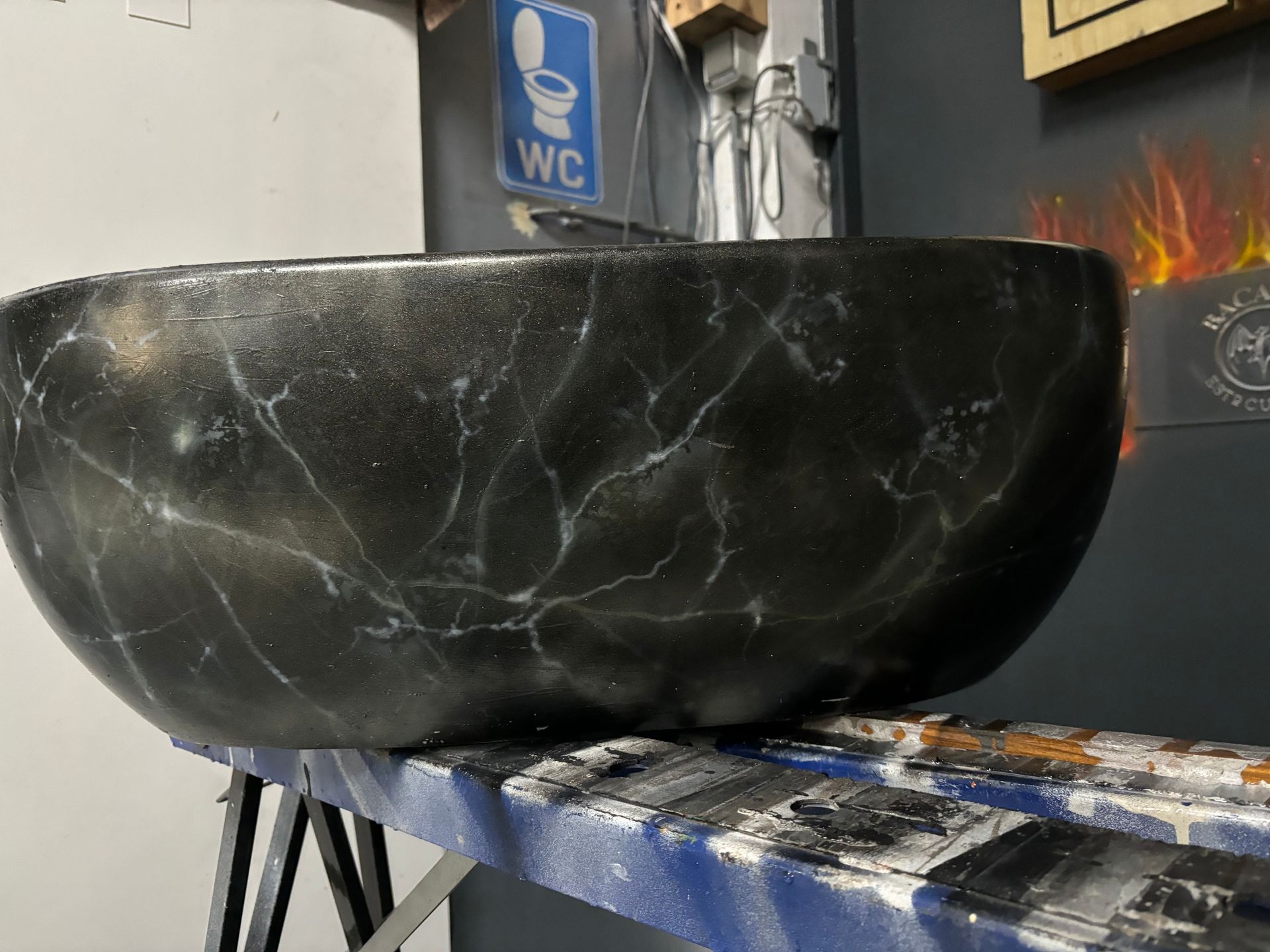 Een zwarte stenen wasbak op een aanrecht in een betegelde kamer, met daarboven een blauw wc-bordje.