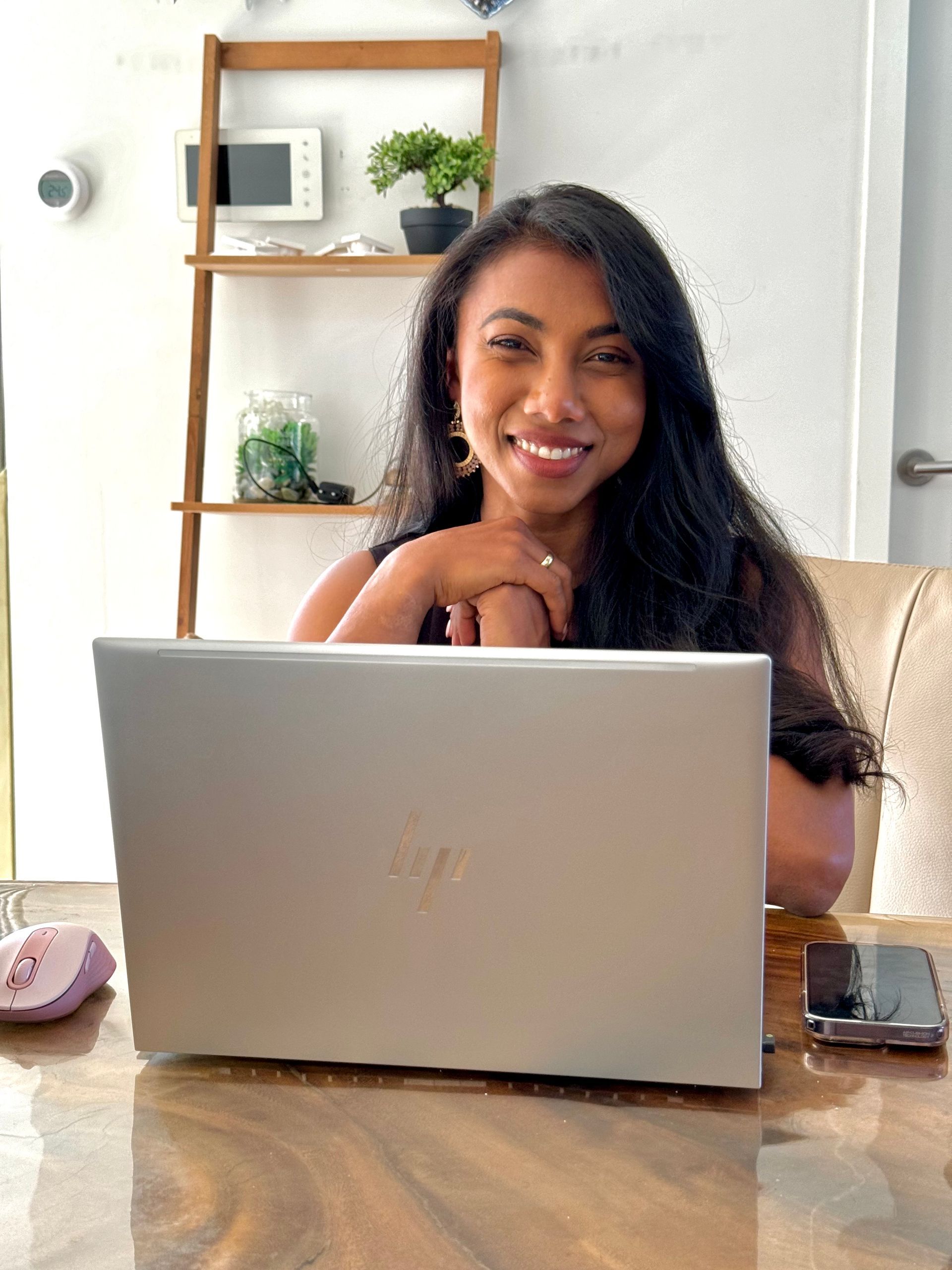 Een vrouw zit aan een tafel met een laptop en lacht