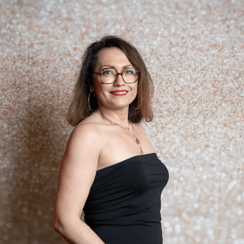 Une femme portant des lunettes et une robe noire se tient devant un mur.