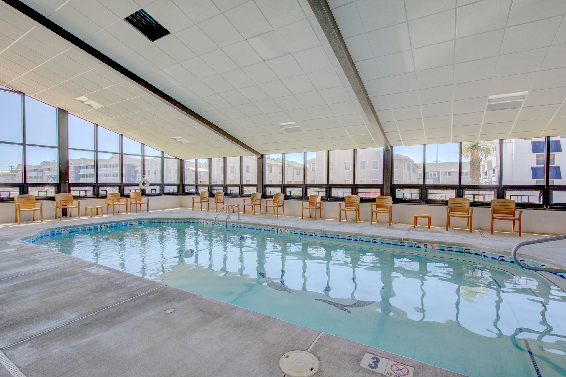 A large indoor swimming pool surrounded by chairs and windows.
