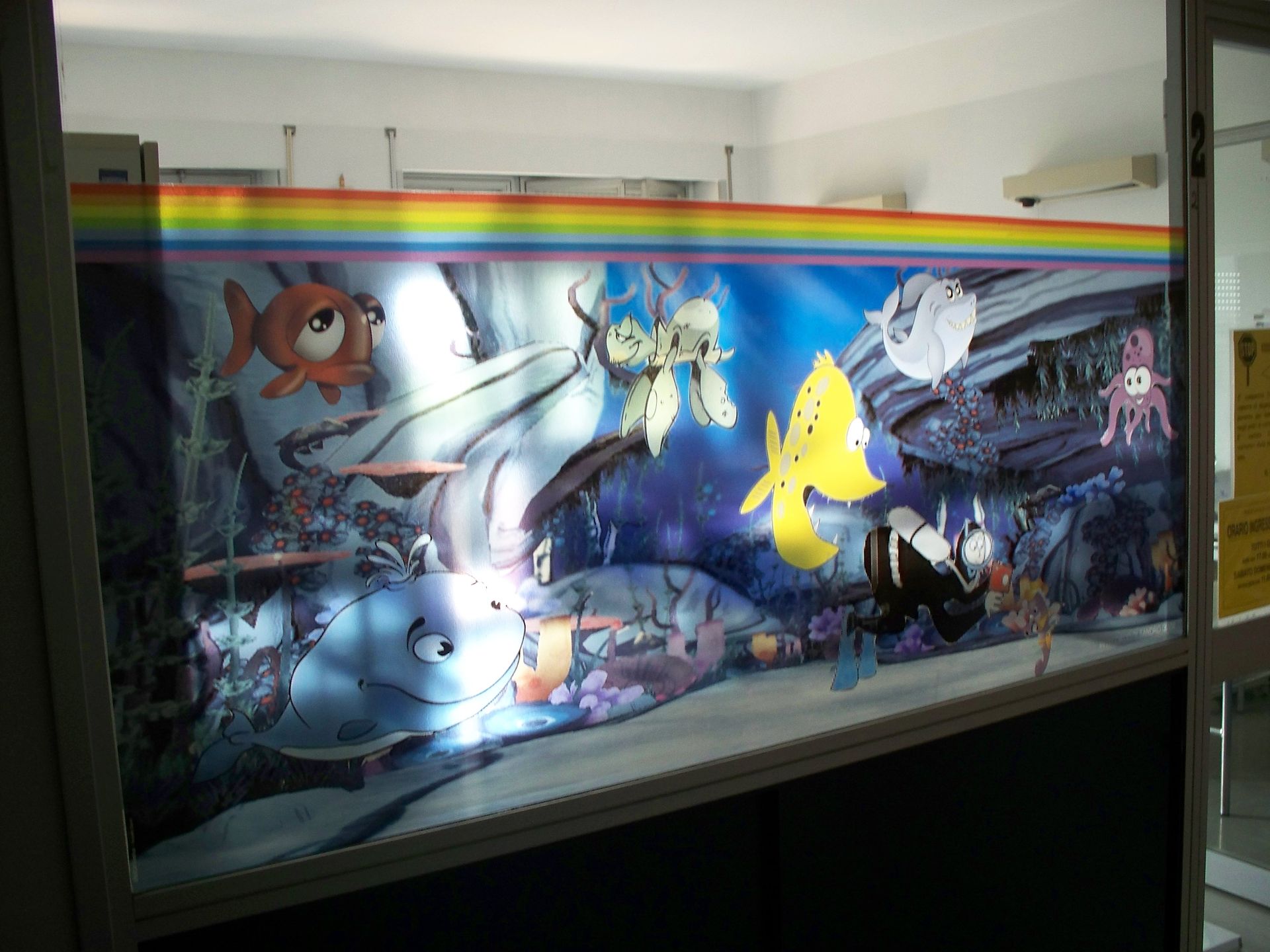 Scena di un pesce in stile cartone animato, blu e colorato, con un arcobaleno sopra, vista attraverso una finestra.