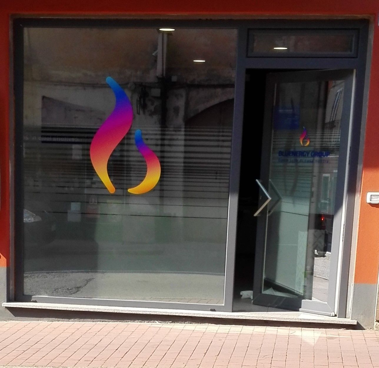 Una vetrina con una porta in vetro parzialmente aperta, su cui è raffigurato il logo di una fiamma nei colori dell'arcobaleno.