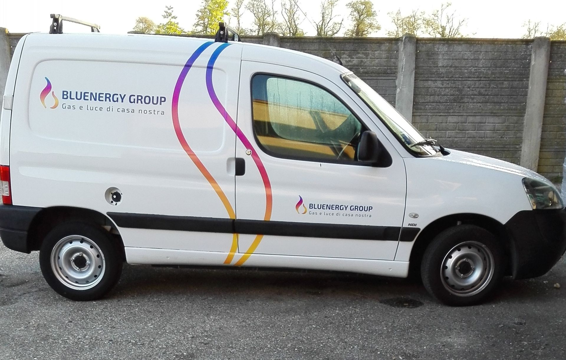 Furgone bianco con logo a spirale blu, viola e giallo; scritta 