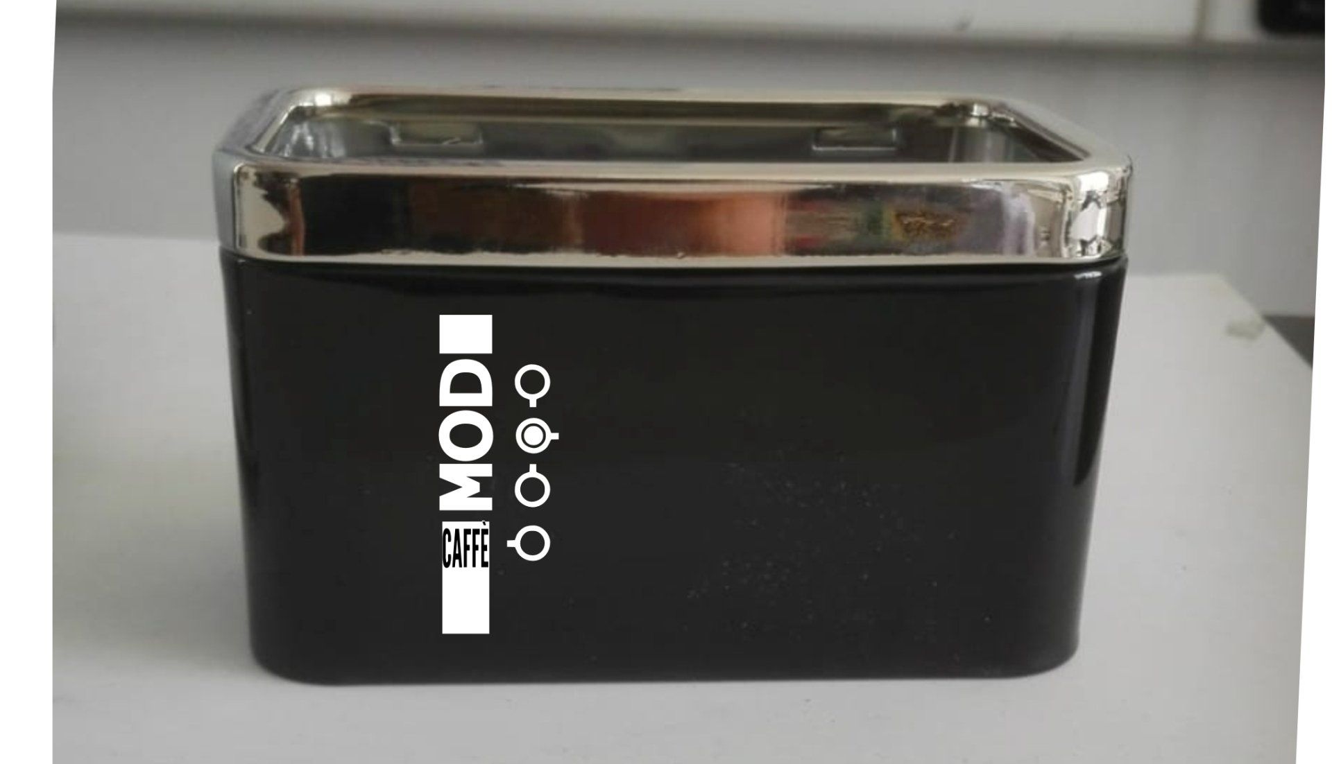 Contenitore quadrato nero con finiture argentate e testo/simboli 