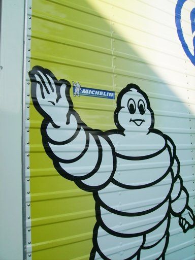 L'omino Michelin su un camion giallo e bianco saluta. È visibile il logo Michelin.