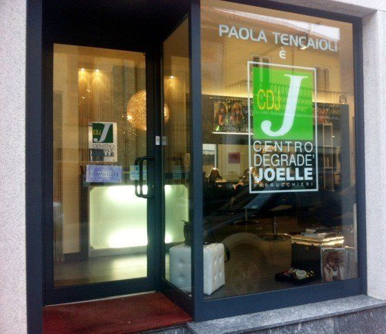 Ingresso del parrucchiere con porta a vetri aperta, segnaletica e vista interna.