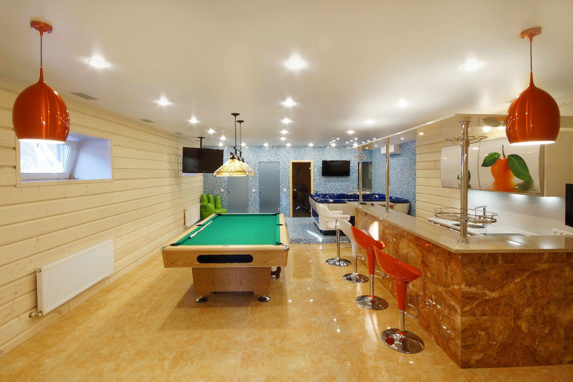 Modern basement rec room with pool table, bar stools, and kitchen counter under pendant lights Modern basement rec room with pool table, bar stools, and kitchen counter under pendant lights