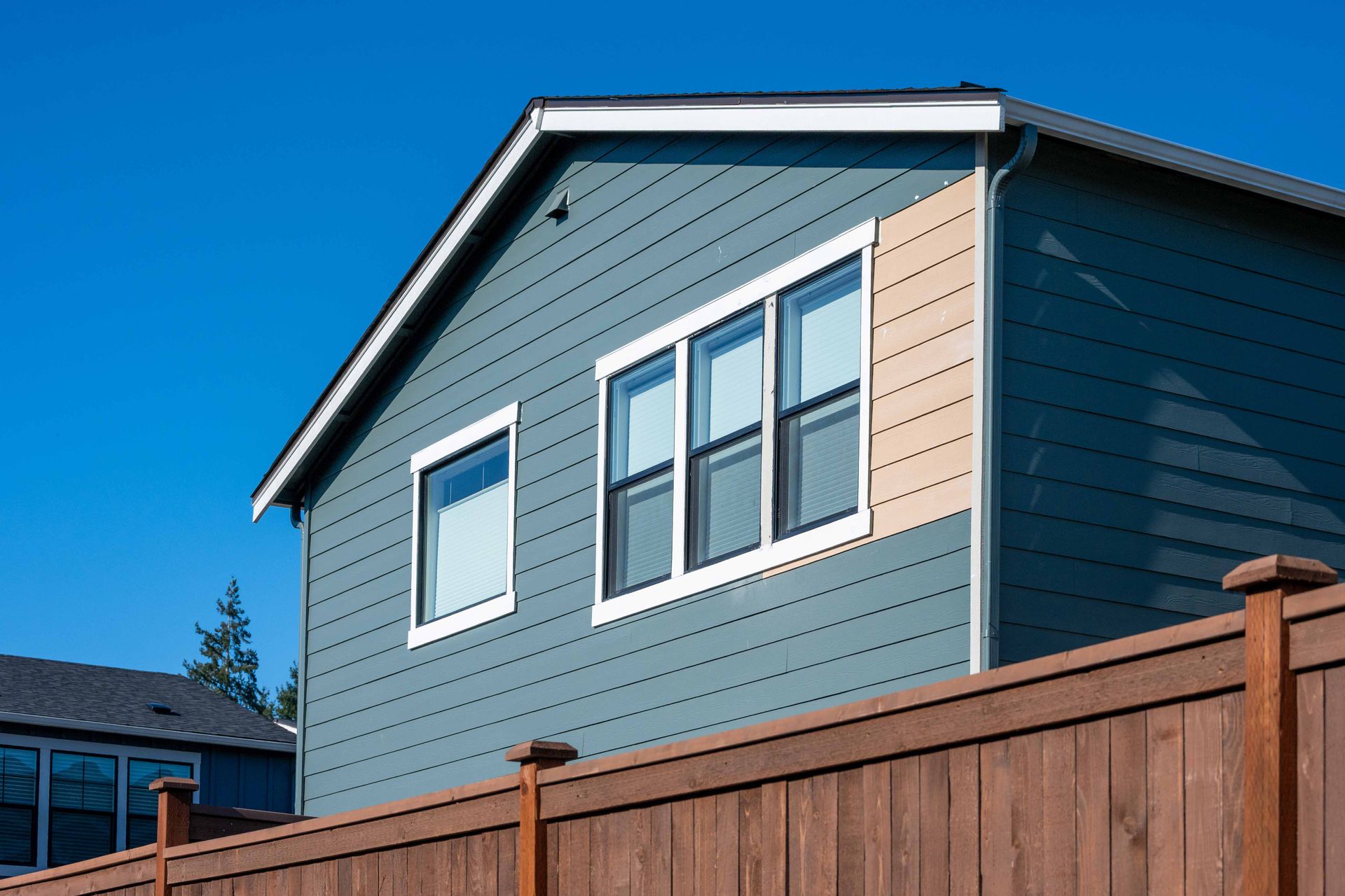 Blue house exterior with gray siding and a wooden fence under a clear sky Blue house exterior with gray siding and a wooden fence under a clear sky