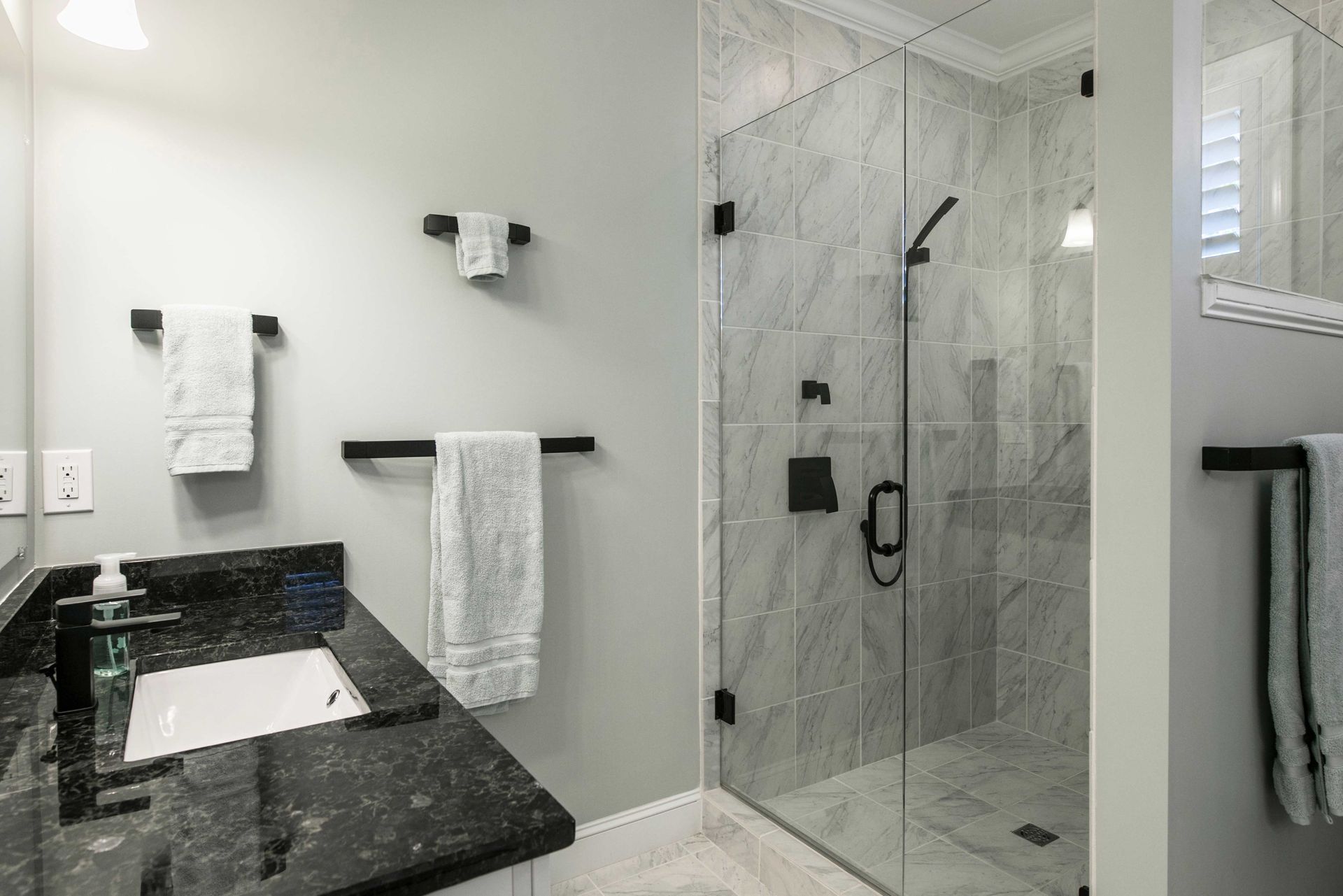 Modern bathroom with black vanity, white towels, and a glass-enclosed marble shower. Modern bathroom with black vanity, white towels, and a glass-enclosed marble shower.