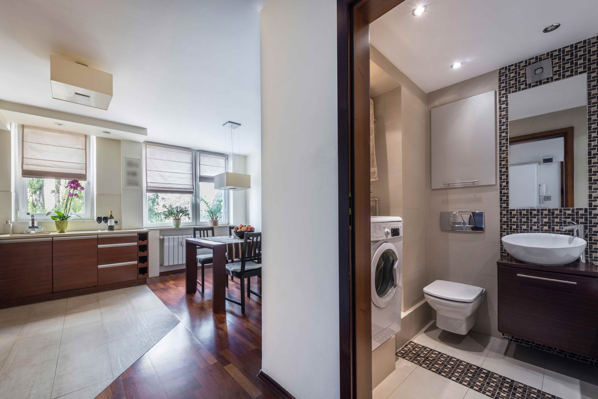 Modern apartment interior with kitchen, dining area, and compact bathroom visible through an open doorway Modern apartment interior with kitchen, dining area, and compact bathroom visible through an open doorway