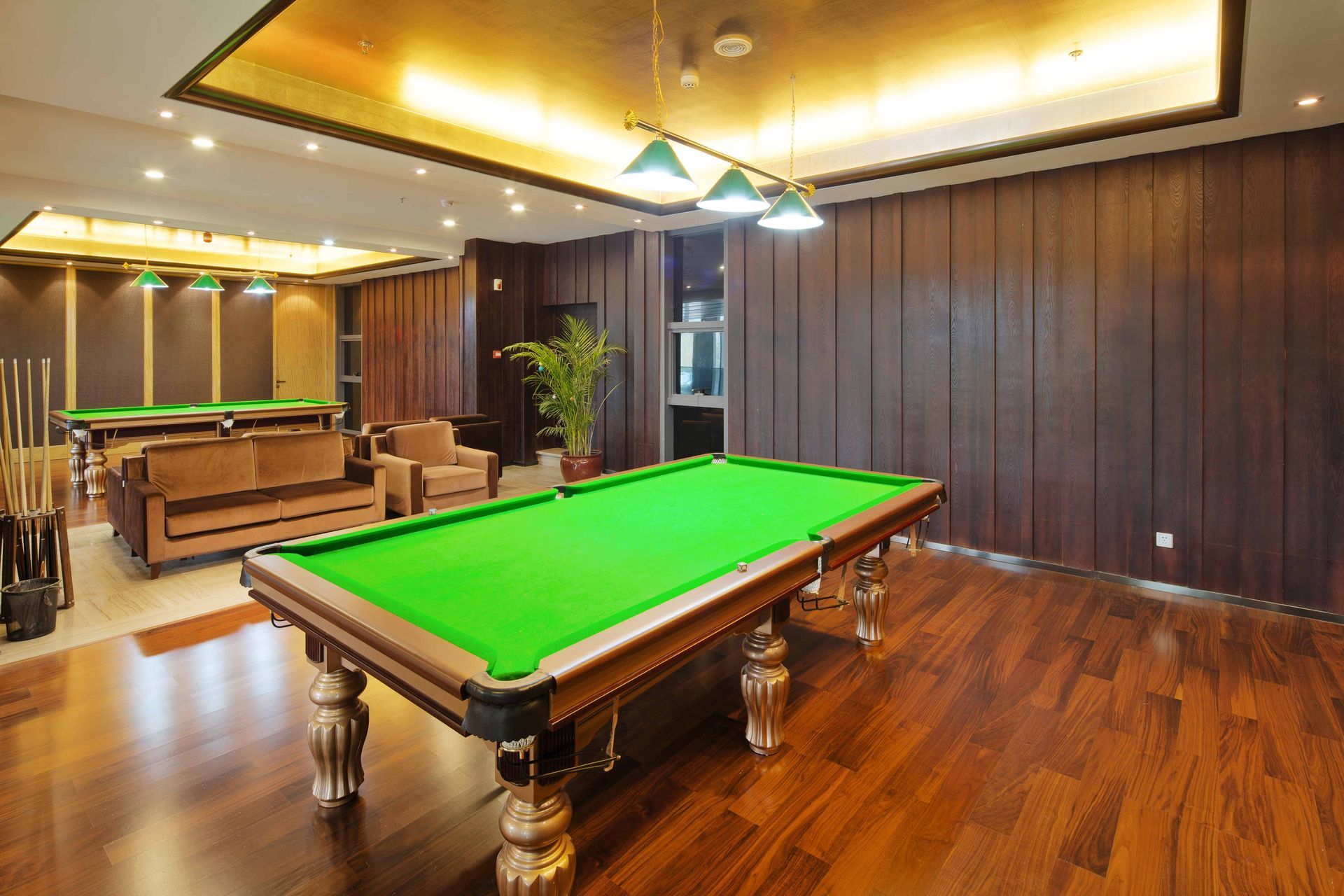Spacious game room with a green pool table, wooden floors, and warm ceiling lights