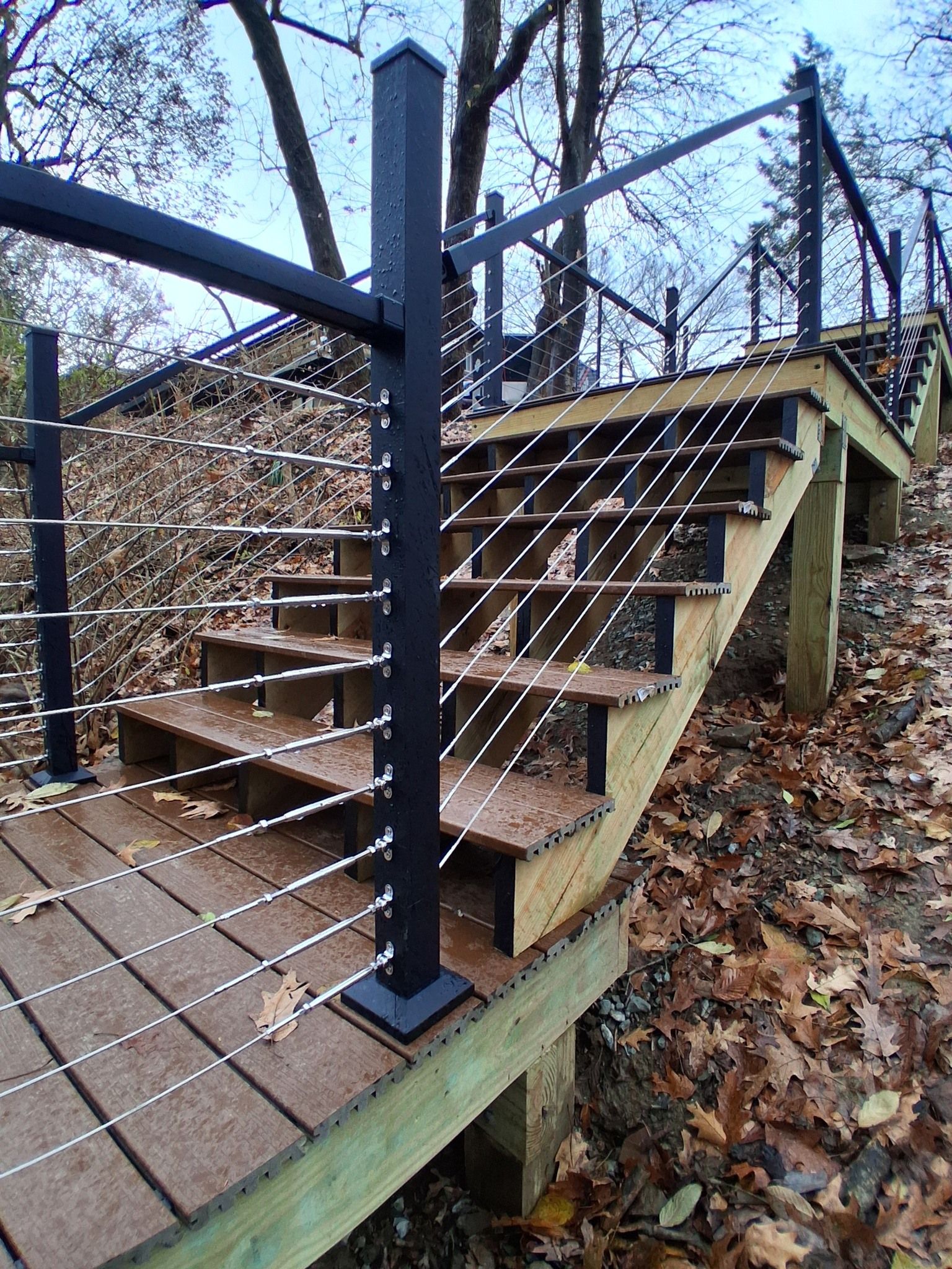 Rusty outdoor metal stairs with black railings and a chain-link fence in a wooded area.