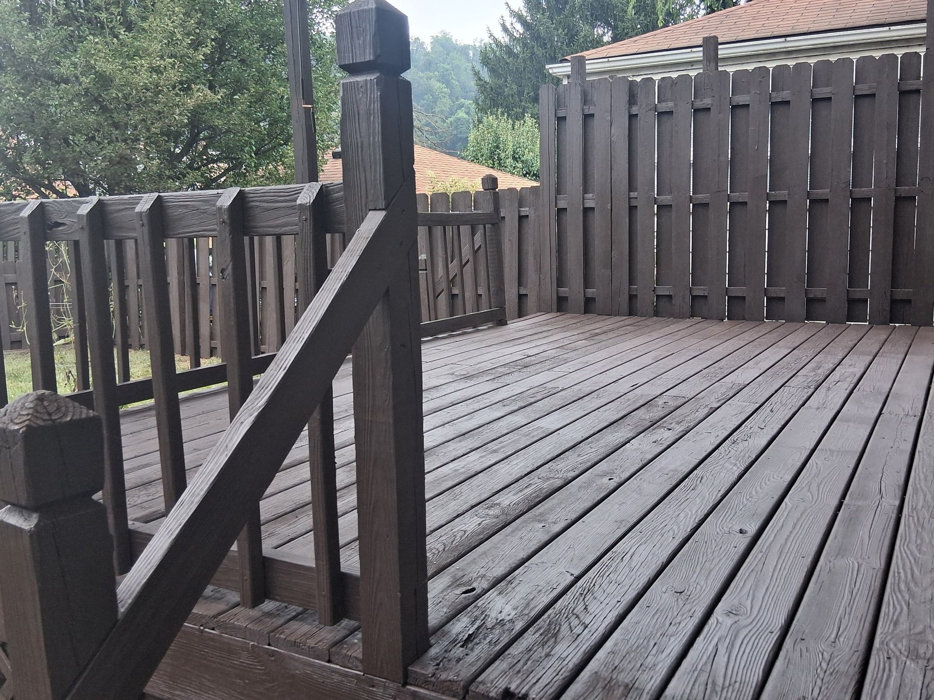 Wooden deck with railings and stairs overlooking a yard and trees