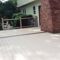 White deck with wooden railing beside a brick house and beige siding, viewed from the corner.