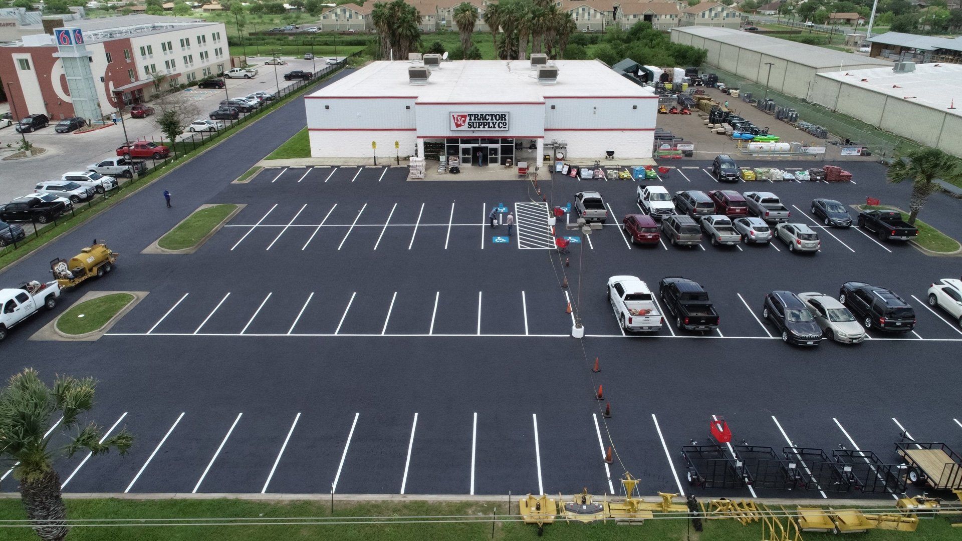 An aerial view of a freshly paved commercial parking lot with white striped spaces and a few parked vehicles.