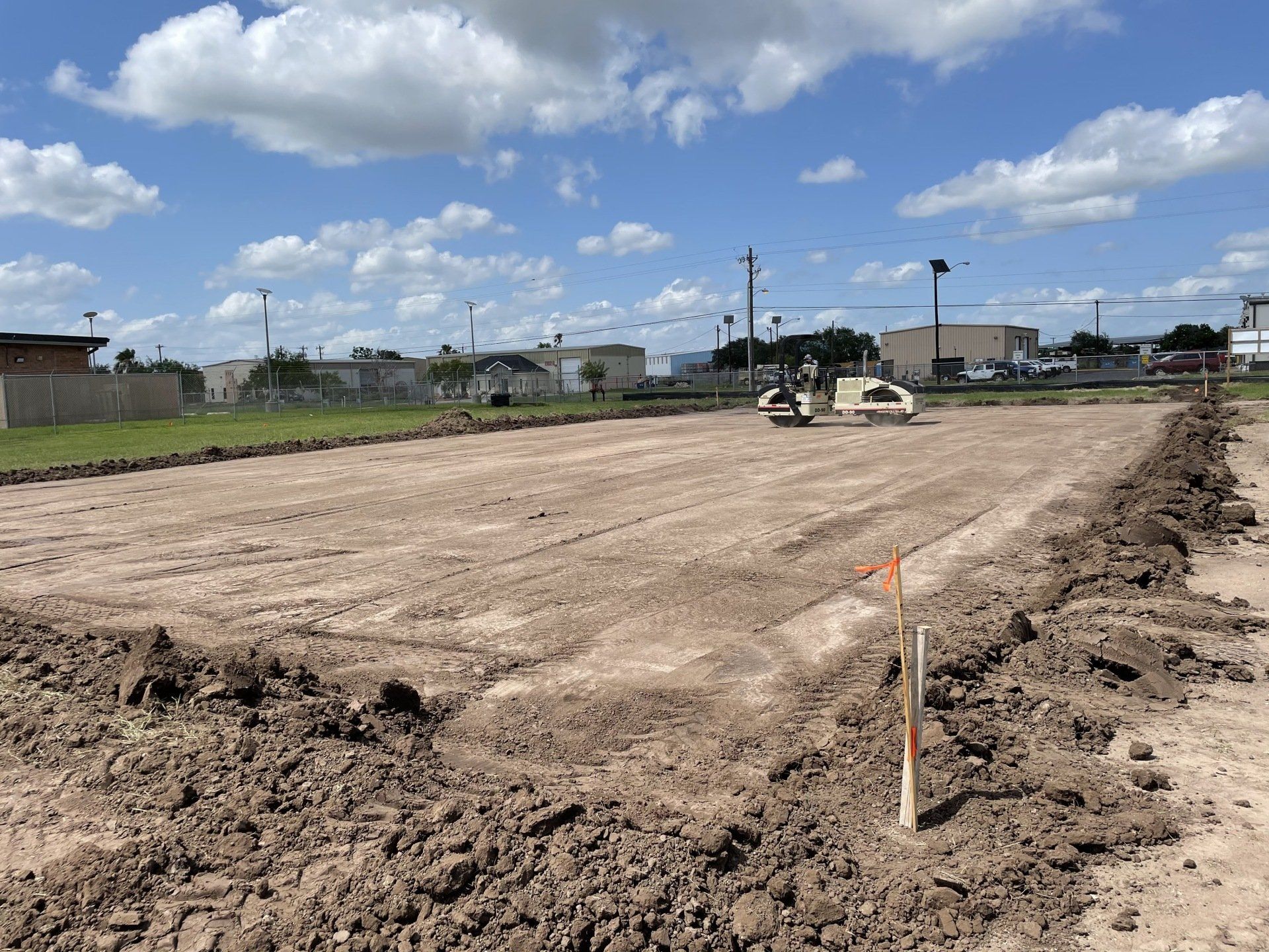 A cleared, leveled construction site with disturbed earth borders, small pieces of equipment, and a blue sky overhead.