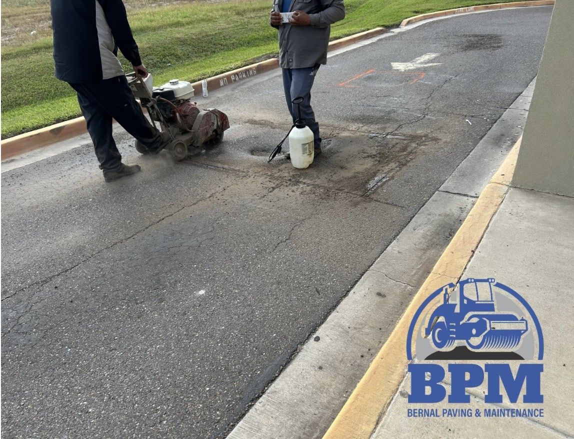 Two workers use a concrete saw to cut into an asphalt road for repair, with a BPM Paving and Maintenance logo in the corner.