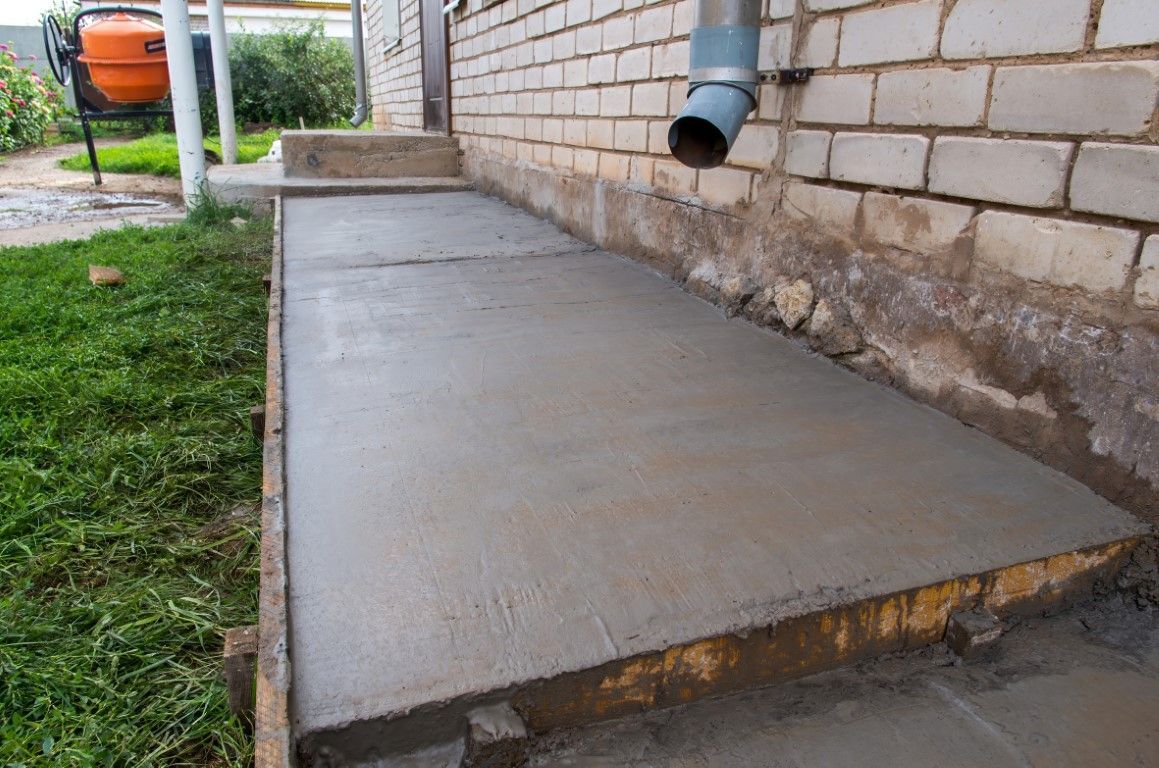 A freshly laid concrete pathway runs alongside a brick building.