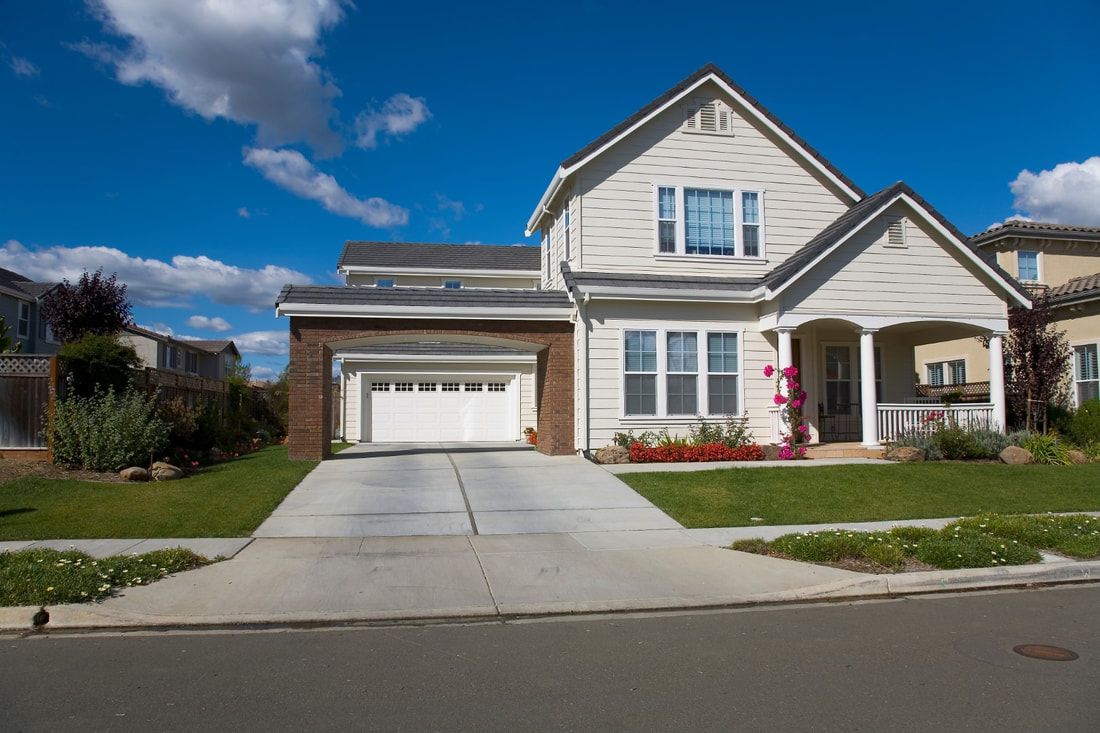 A modern suburban house with a white facade and brick trim, featuring a two-car garage, manicured lawn.