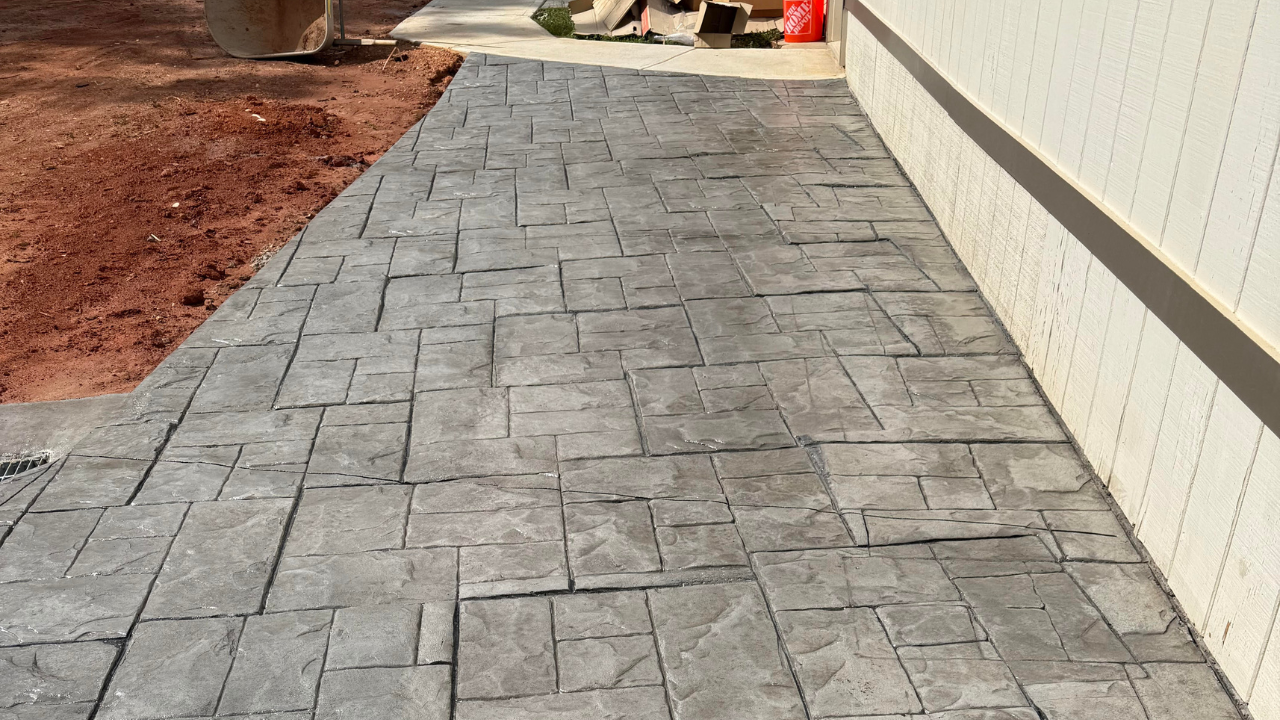 Concrete pathway with a stamped brick pattern next to a beige siding wall. 