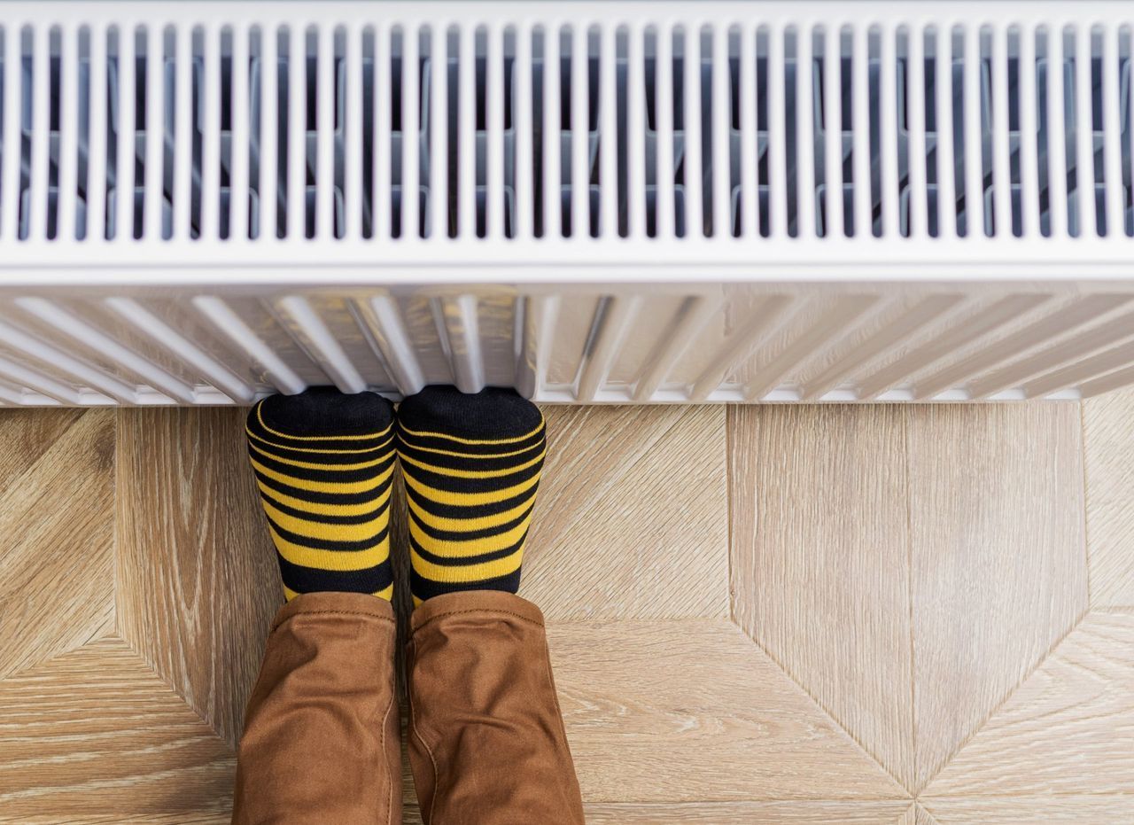 A person wearing striped socks is standing next to a radiator.