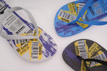 Un par de zapatillas negras texturizadas con un corazón blanco y un nombre bordados, sobre un suelo de madera.