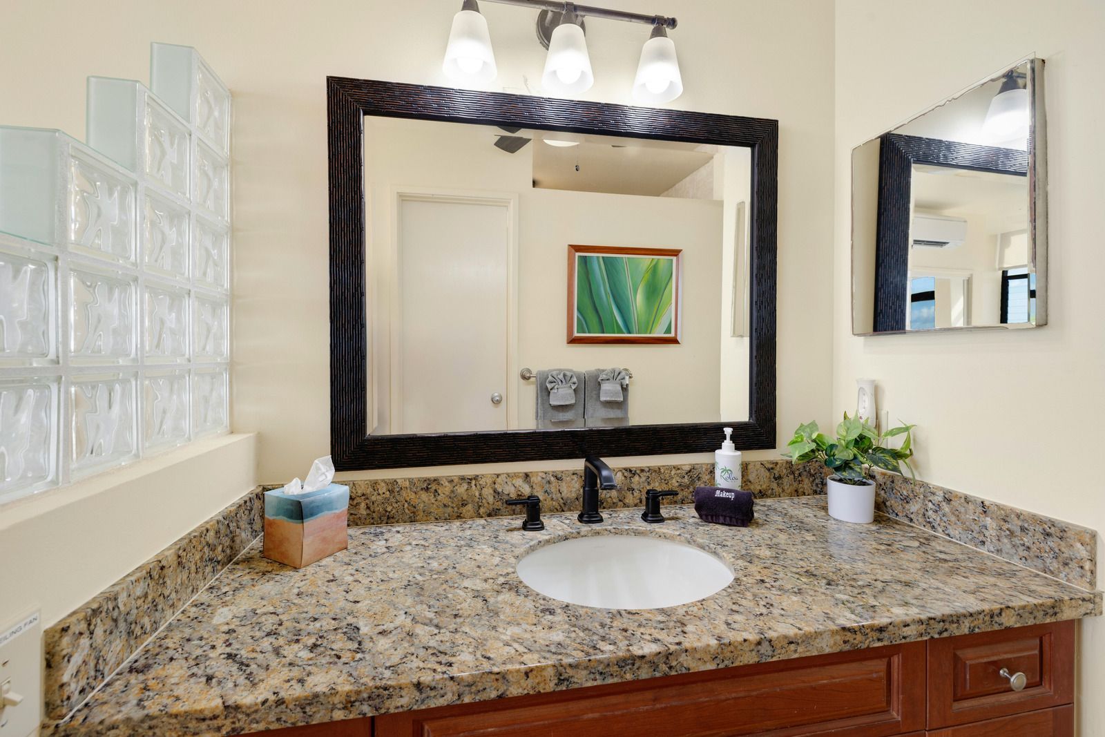 Bathroom with granite countertop, large mirror, and glass block wall.