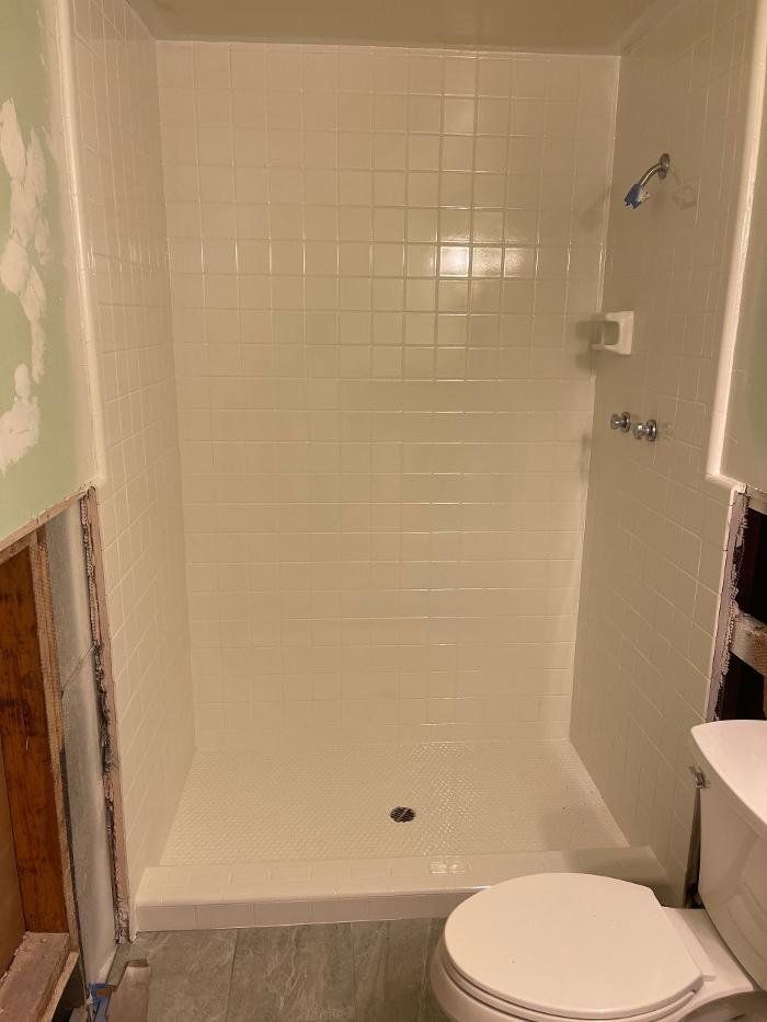 White tiled shower stall with a toilet in a bathroom.