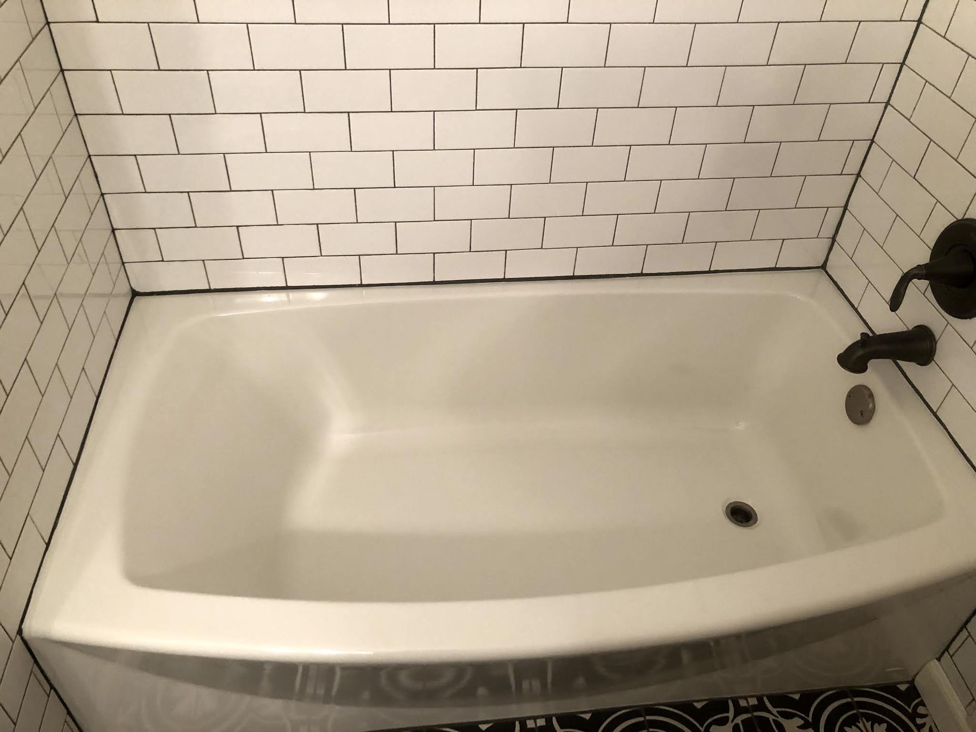 White bathtub with black fixtures, surrounded by subway tile in a bathroom.
