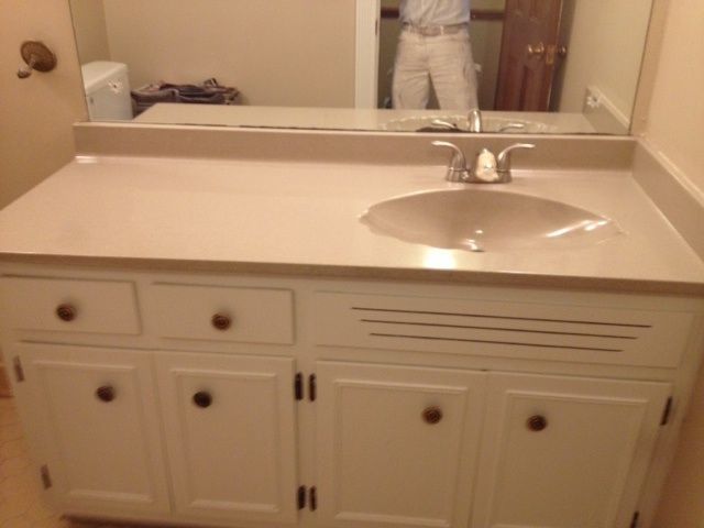 White bathroom vanity with tan countertop and sink, mirror, person in doorway.