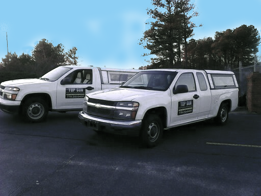 Two white Chevrolet pickup trucks with camper shells parked outdoors; blue sky background.