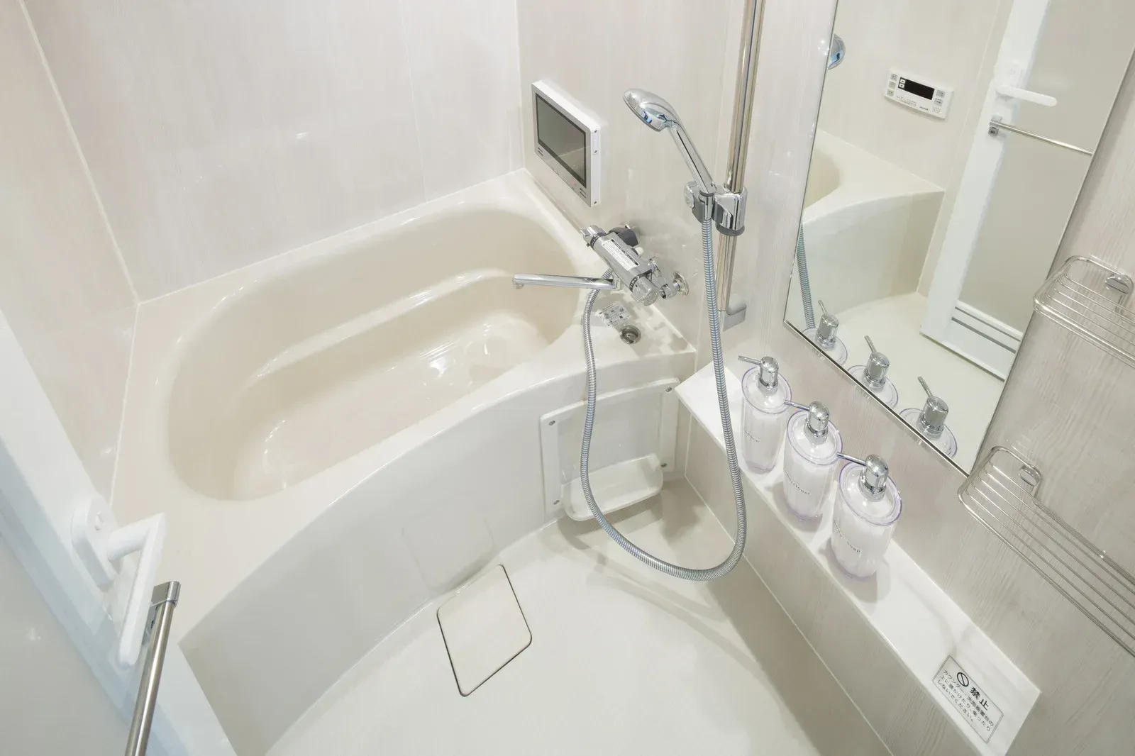 Small, modern bathroom with a white bathtub, shower, and mirror.