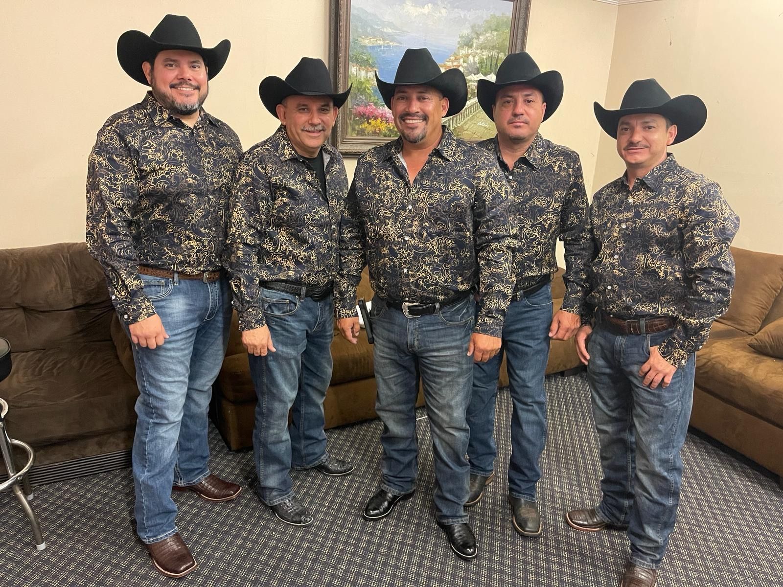 Grupo Orgullo wearing cowboy hats are standing next to each other in a living room.